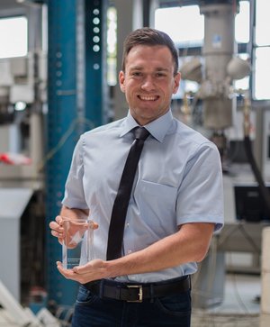 Dr.-Ing. Stefan Käseberg mit dem Dissertationspreis 2017 in einem Laborraum. Der Preisträger steht im Labor und hält den Glas-Dissertationspreis in der Hand