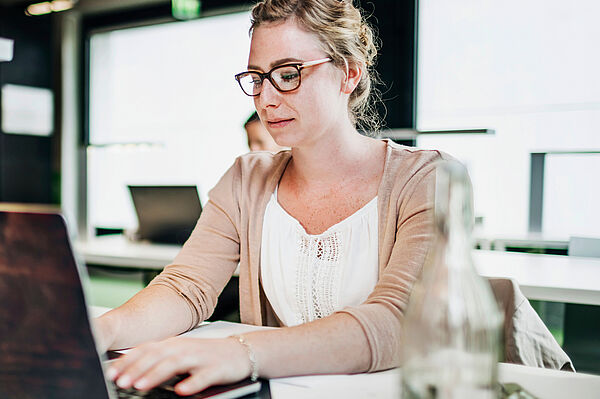Junge Frau sitzt am Laptop. Sie hat die Hände auf der Tastatur.