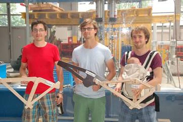Drei Personen stehen in einem Labor und halten Modelle aus Holz in den Händen, sie blicken in die Kamera. 