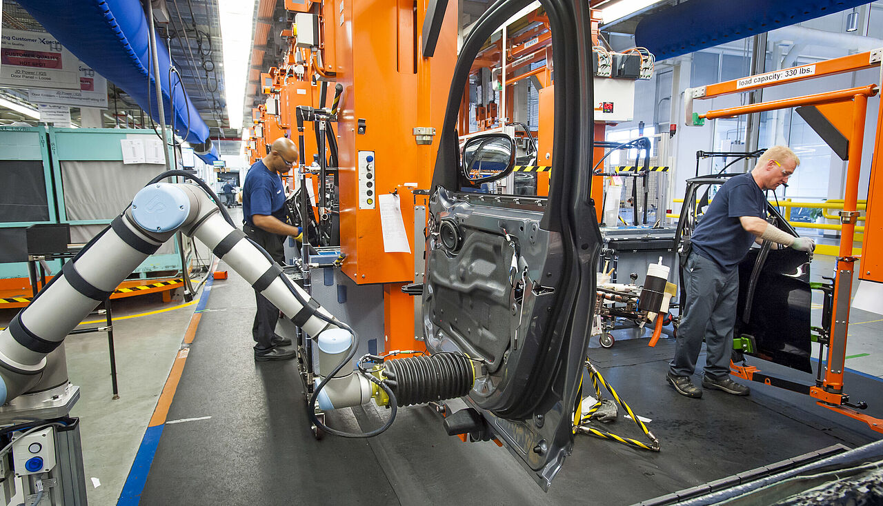 Menschen und Maschinen arbeiten in einer Produktionsanlage gemeinsam an der Fertigung von Fahrzeugen