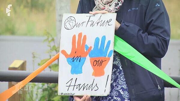 Hände halten ein bemaltes Plakat, darauf sind 2 Hände zu sehen und der Text "Our future in our hands"