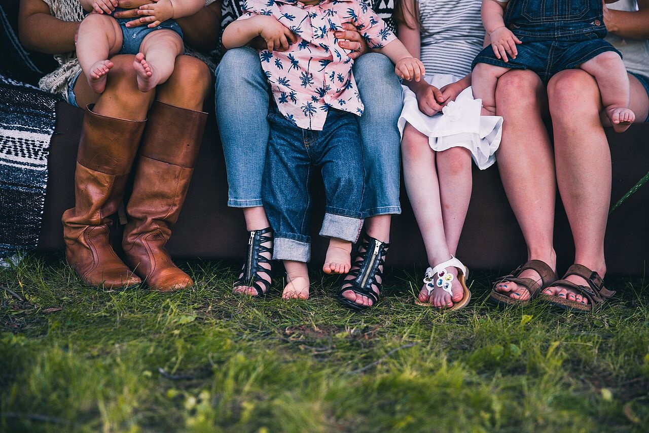 Eine Familie sitzt auf einer Bank auf einer Wiese. Zu sehen sind nur die Beine.