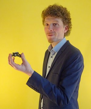 Dissertationspreisträger 2023 Dr. Raphael al Diban ein Mann hält vor einer gelben Wand ein CD-Lesegerät in der Hand