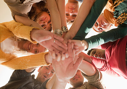 Willkommenskultur leben: Mentor werden! Neun Junge Leute im Kreis stehend legen ihre Hände zusammen in die Mitte