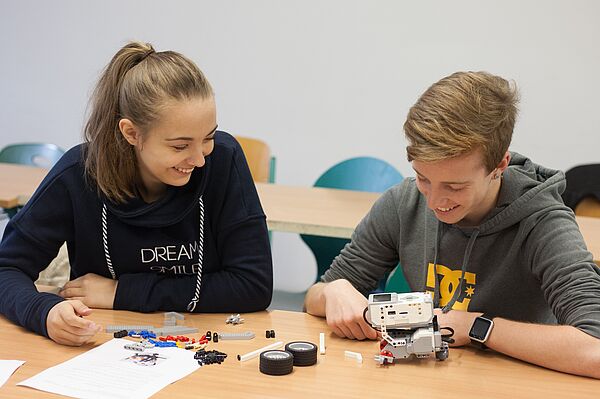 Ein Junge und ein Mädchen sitzen an einem Tisch und basteln an einem Lego-Roboter