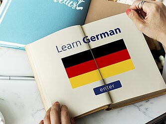 Offenes Buch mit Überschrift "Learn German" und einer deutschen Flagge