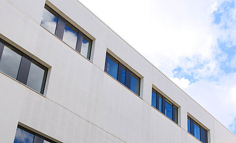 HTWK Medienzentrum (Foto: Swen Reichhold) Außenfassade eines grauen Gebäudeblocks mit mehreren rechteckigen Fenstern. Im Hintergrund ist der Himmel zu sehen.