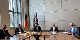 5 Personen an Konferenztisch bei Unterzeichnung eines Papiers