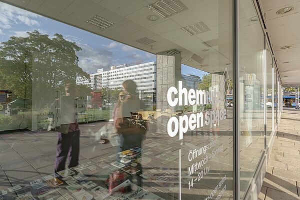 Spiegelung in einer Scheibe: Menschen und Schrift "Chemnitz open Space")