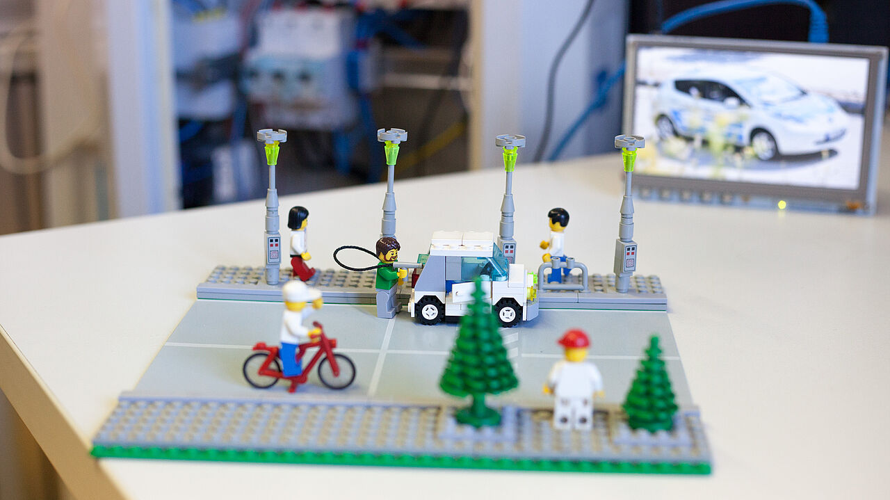 Ein Lego-Modell einer Straße mit Elektroautos, Laternen und Fahrradfahrer