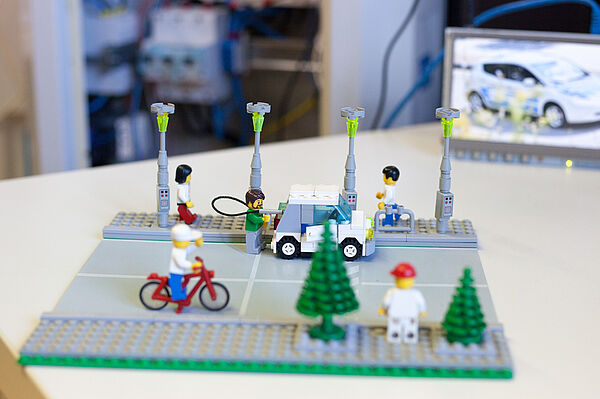 Ein Lego-Modell einer Straße mit Elektroautos, Laternen und Fahrradfahrer