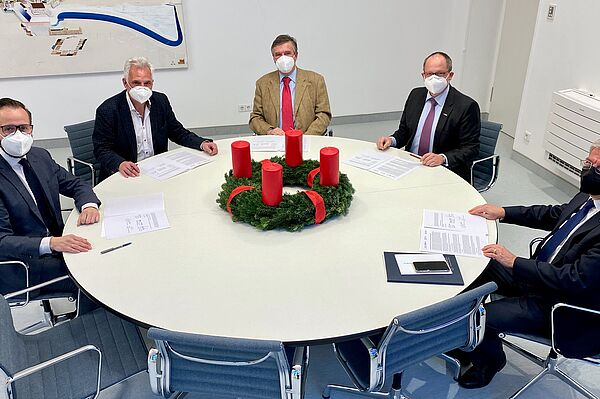 5 Herren mit Papieren & mit Masken an rundem Tisch