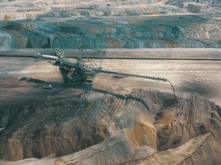 SIMPeL A large construction vehicle in a terraced opencast mine, seen from a bird’s-eye view, surrounded by layers of earth
