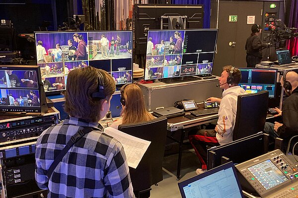 Personen in einem Regie-Raum mit vielen Bildschirmen