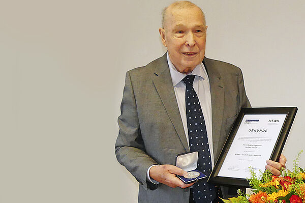 Dr. Staude festlich gekleidet im Anzug mit einer Urkunde in der linken und der Albert-Geutebrück-Medaille in der rechten Hand.