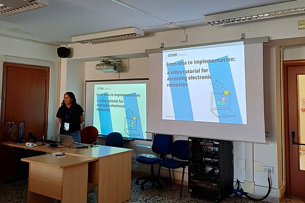 Eine Frau steht vor einer Beamer-Präsentation für ein Tutorial zur Nutzung elektronischer Medien.