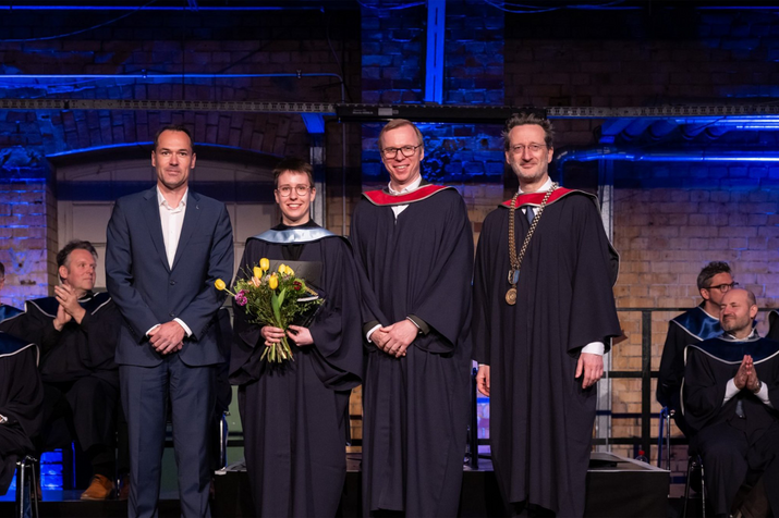 Gruppenfoto auf der Bühne, Preisträgerin im Talar hält Blumen in der Hand