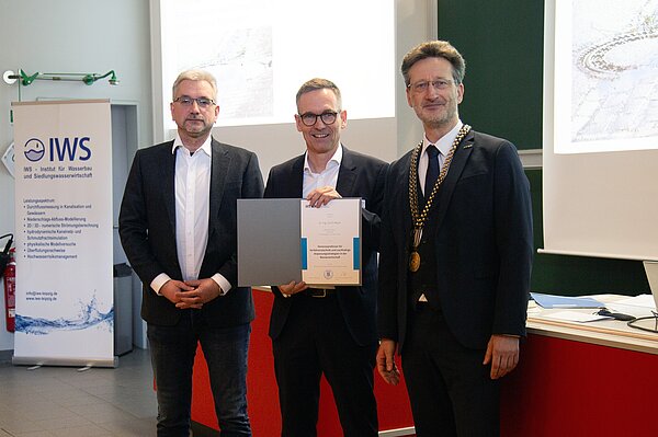 Honorarprofessor Dr. Ulrich Meyer berufen drei Männer in Anzügen stehen zusammen, der Mittlere hät eine Urkunde hoch