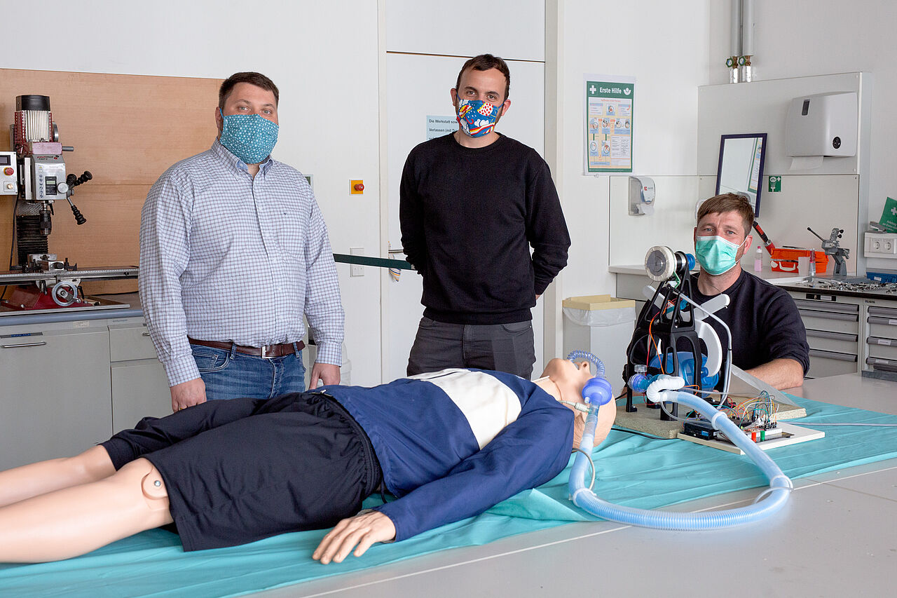 Dr. Hans-Martin Dörfler, Andreas Blum und Frank Schmidt hinter einer medizinischen Puppe, die an das entwickelte Beatmungsgerät angeschlossen ist. 