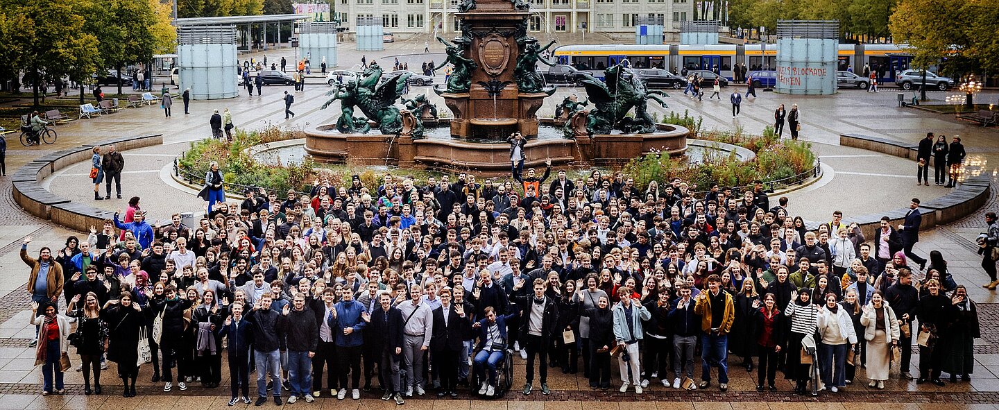große Menschengruppe auf Stadtplatz vor Obelisk und Brunnen mit Gebäuden im Hintergrund