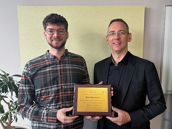zwei Männer halten einen Award in den Händen