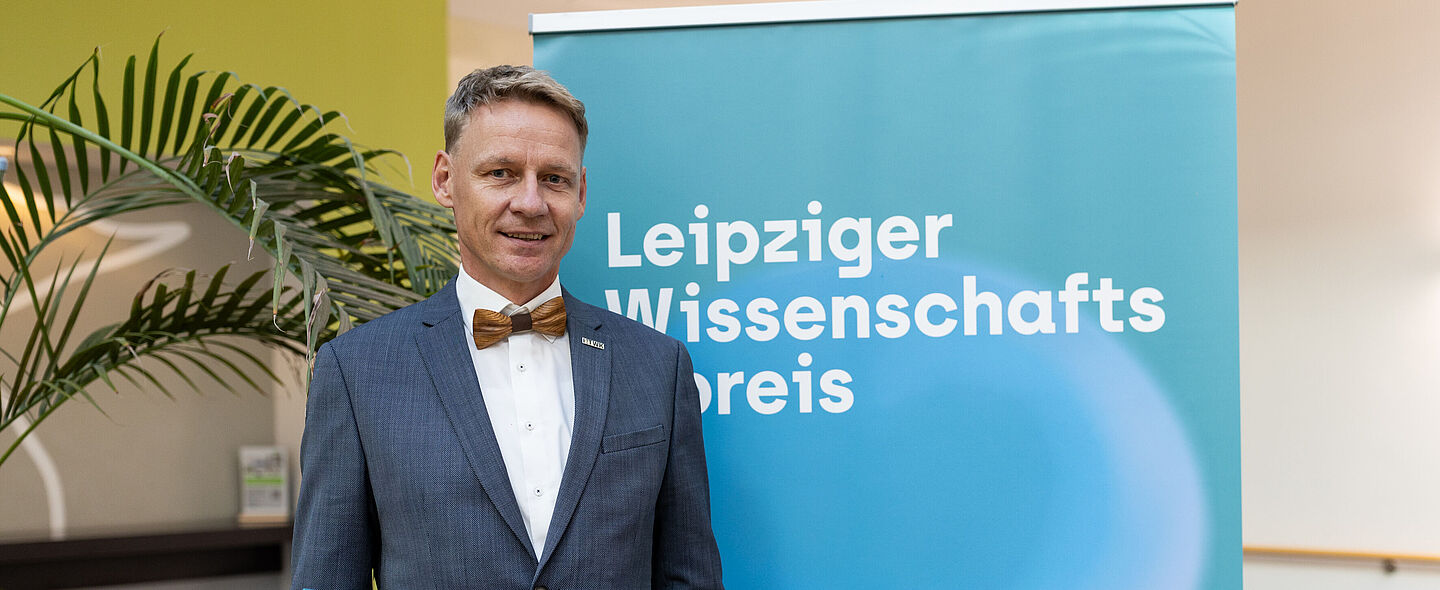 Mann mit Urkunde steht vor Plakat