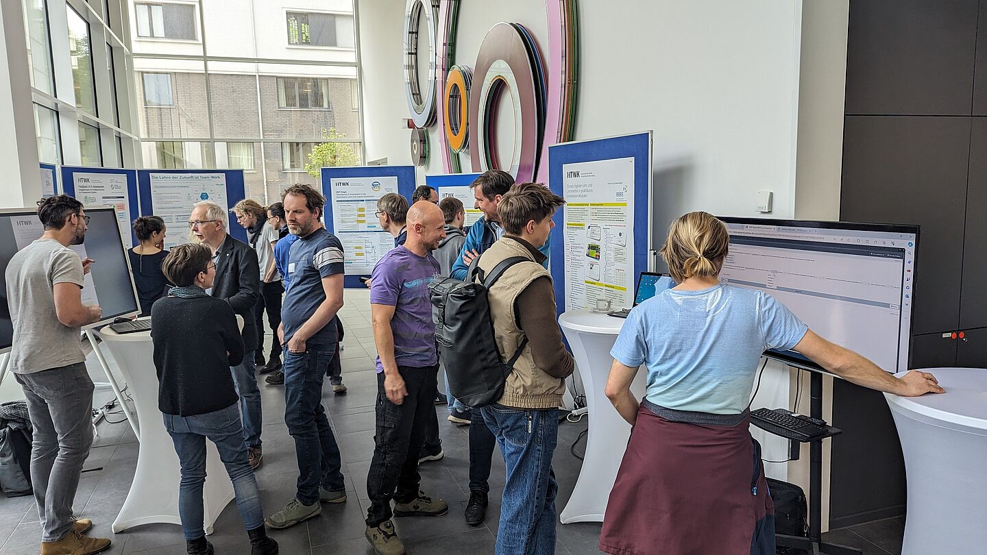 Personen stehen vor Informationstafeln und unterhalten sich im Foyer eines Hochschulgebäudes.