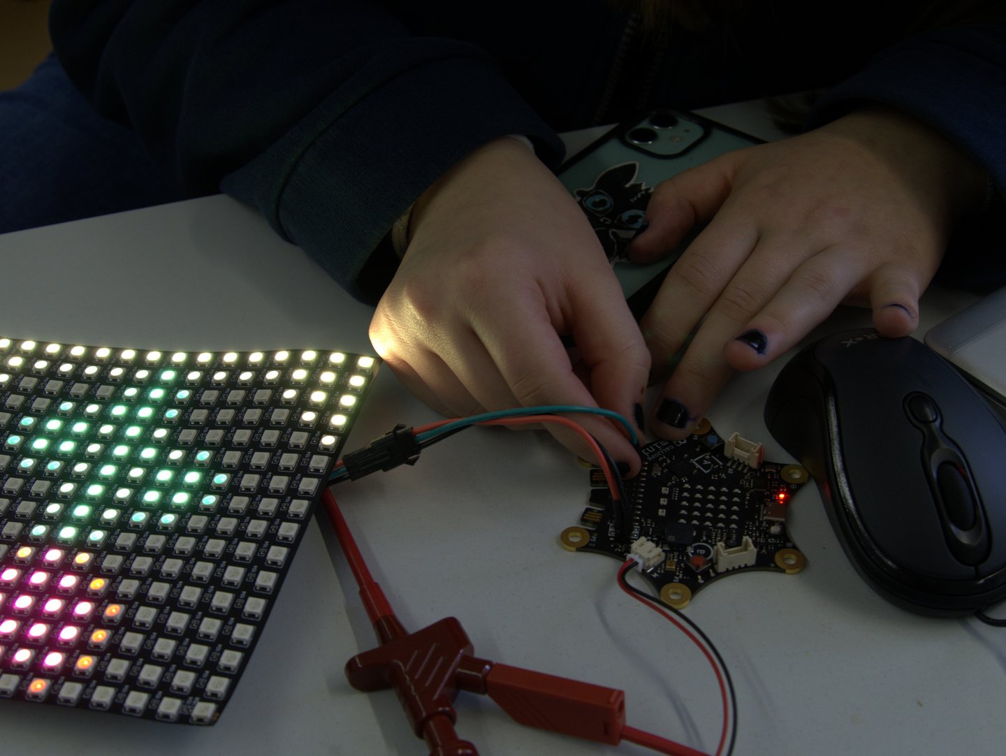 Hände verkabeln einen Calliope und daneben liegt eine Pixelmatte mit einer aufleuchtenden LED Blume