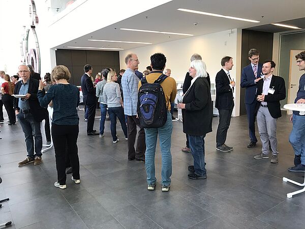 Leute unterhalten sich an Stehtischen im Foyer.