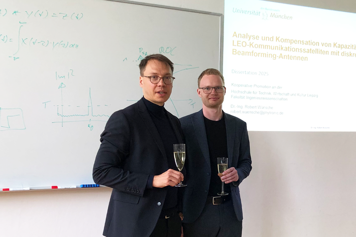 Prof. Krondorf und Prof. Wünsche mit einem Glas Sekt in der Hand schauen in die Kamera