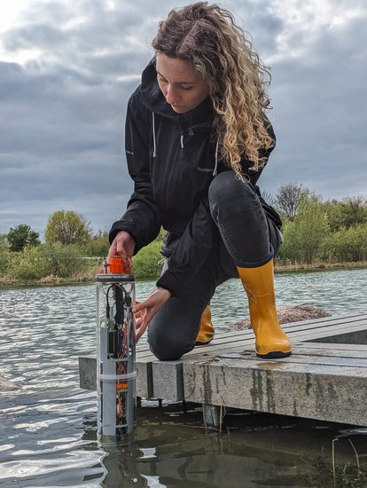 Stefanie kniet und hält Messgerät ins Wasser