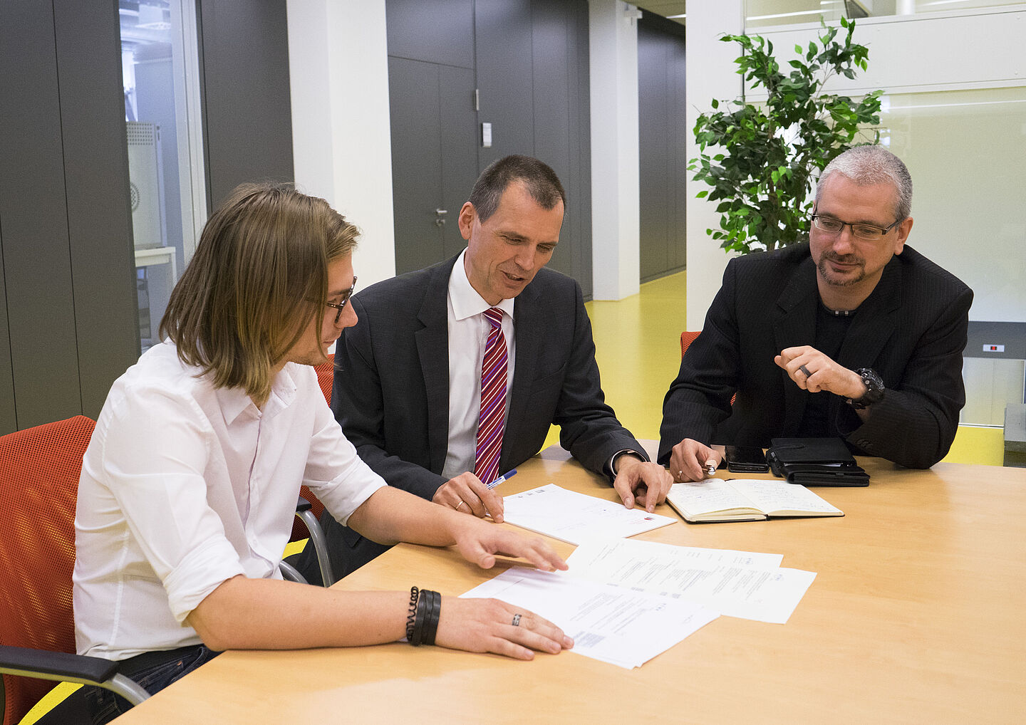 Ein Doktorand sitzt mit zwei Professoren an einem Tisch und bespricht mit ihnen ein Paper.