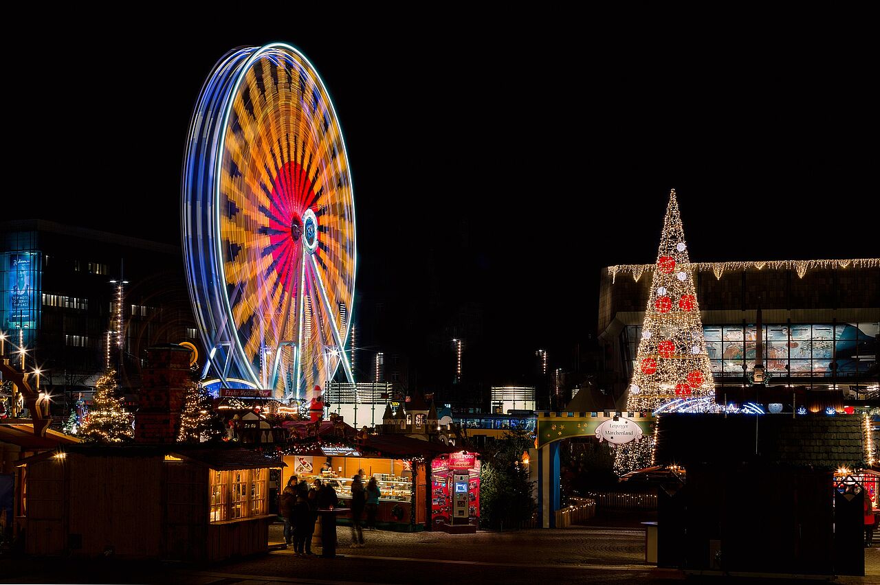 Nachtaufnahme vom Augustusplatz zu Zeiten des Weihnachtsmarktes, also mit mit erleuchteten Buden und in farbiges Licht getauchtes Riesenrad.