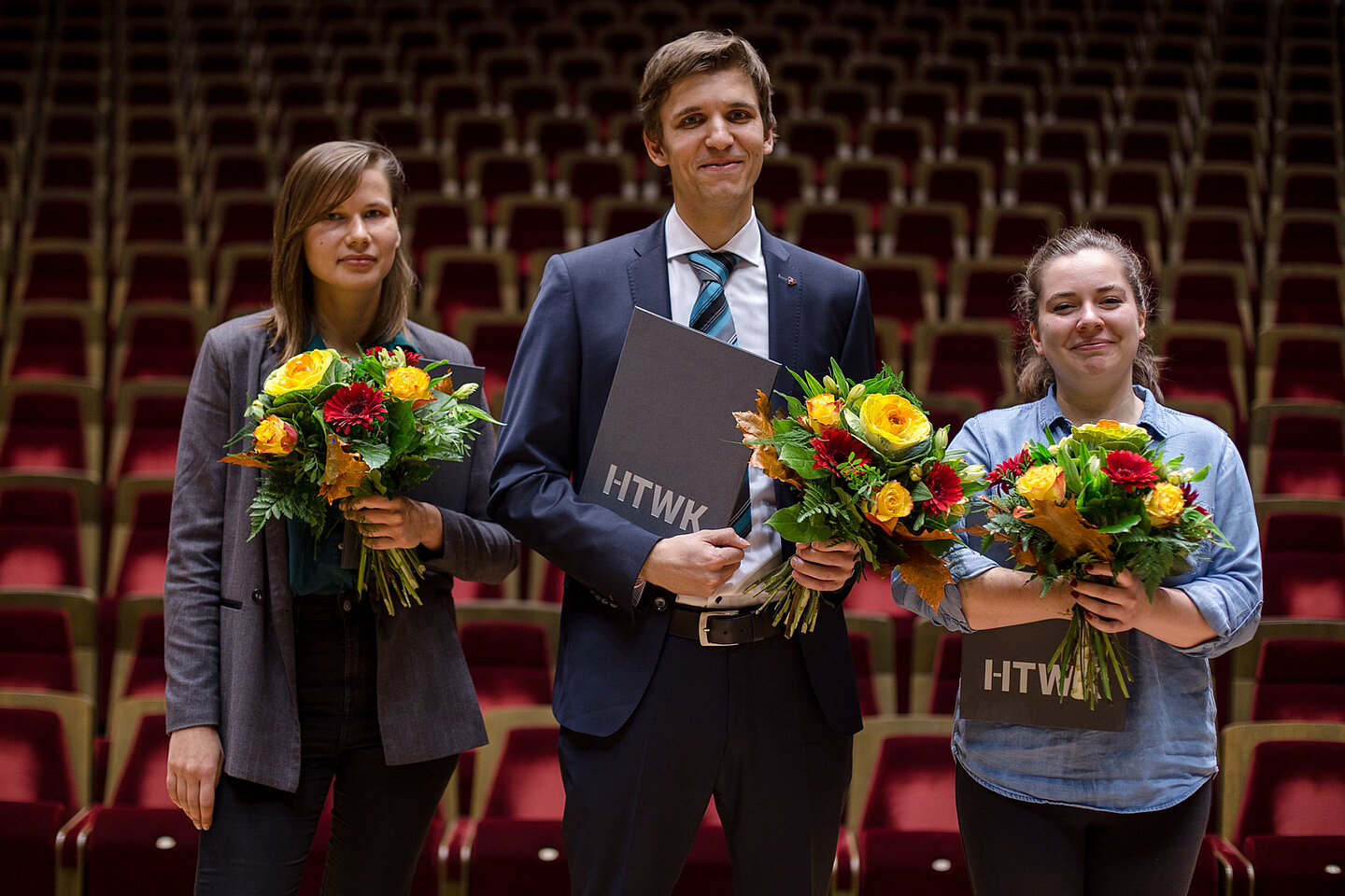 Zwei Frauen und ein Mann je mit Blumenstrauß in der Hand stehen auf der Bühne im großen Saal des Gewandhauses