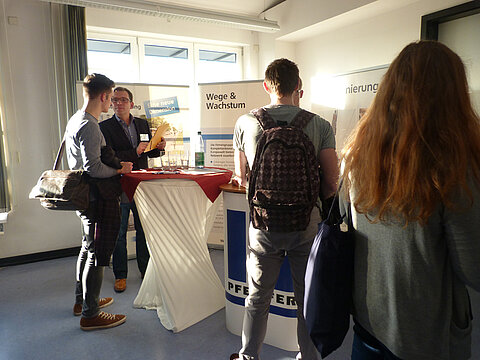 Student unterhält sich mit einem Mitarbeiter eines Kooperationsunternehmens.