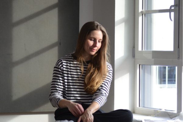 Andréa Hugen sitzt auf einer Holzkiste vor dem Fenster und schaut nach unten..