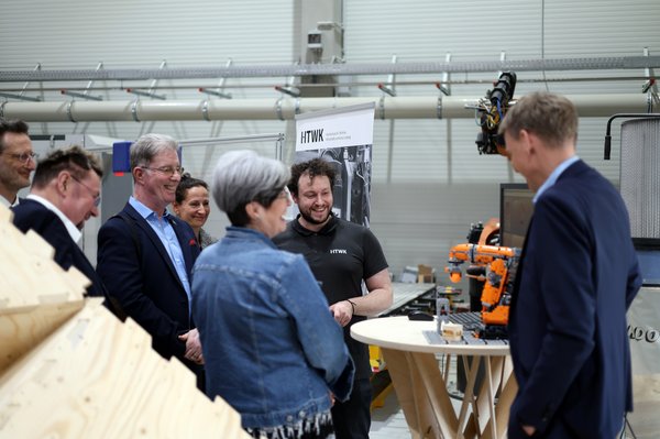 mehrere Personen schauen auf ein Robotermodell in einer Halle