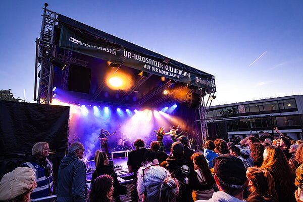 Live-Musik auf der Bühne des Festivals „Leipzig zeigt Courage“. Ein Blick aus der Besuchermenge auf die Bühne des Festivals bei Sonnenuntergang.