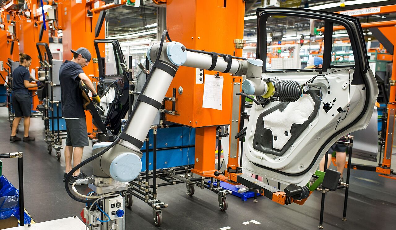 Menschen und Maschinen arbeiten in einer Produktionsanlage gemeinsam an der Fertigung von Fahrzeugen