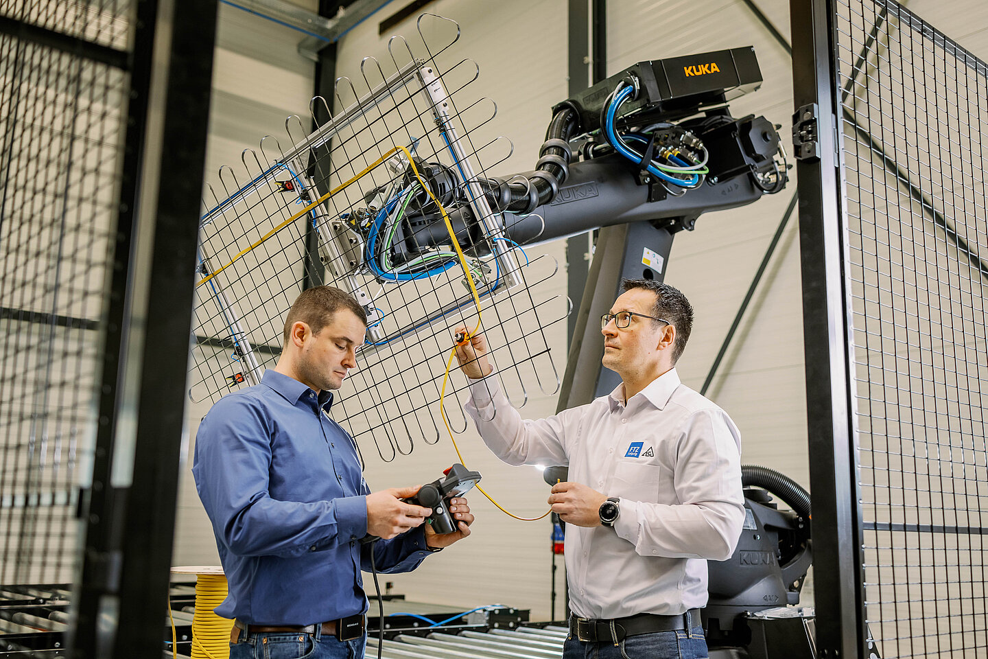zwei Männer stehen in einer fertigungshalle vor einem Roboterarm