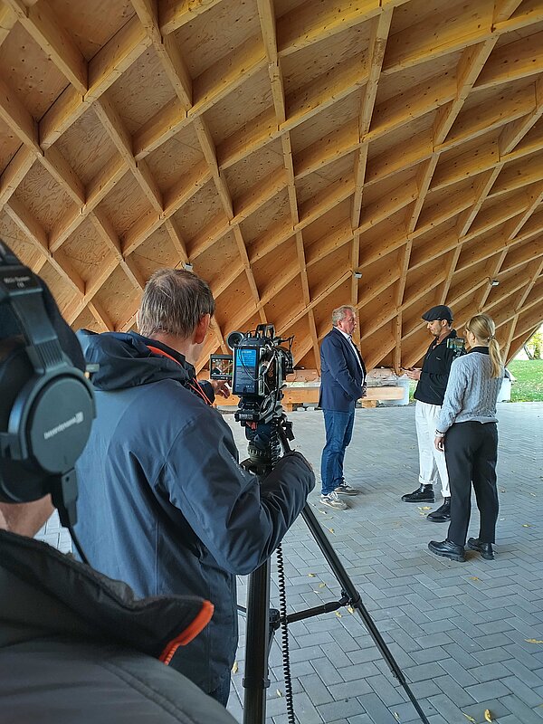 Menschen stehen für einen Videodreh unter einer Holzdachkonstruktion