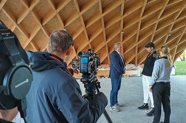 Menschen stehen für einen Videodreh unter einer Holzdachkonstruktion