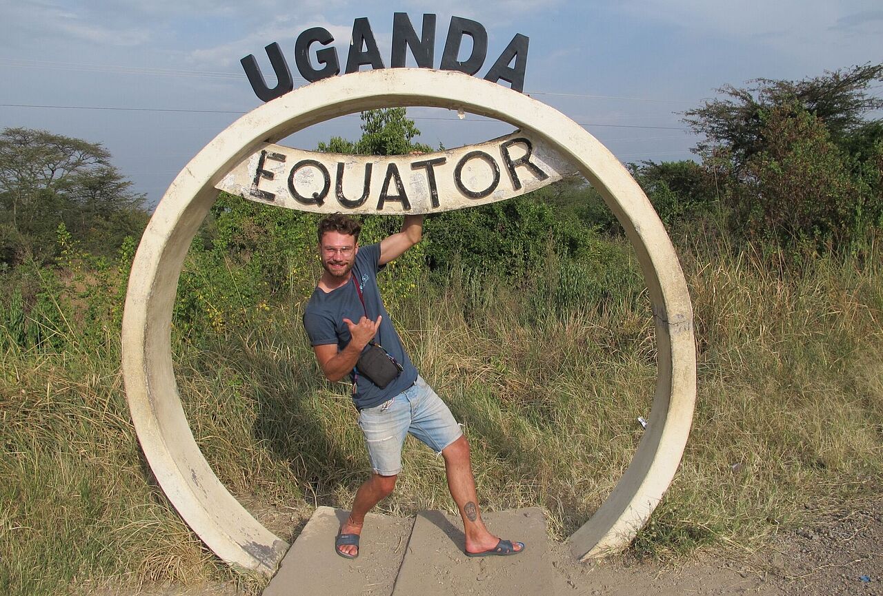 Ruben Gerstner steht lässig in einem kreisförmigen Symbol, das mit dem Schriftzug „Uganda Equator“ auf den Verlauf des Äquators an dieser Stelle hinweist.