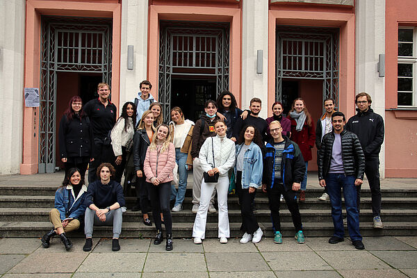 Gruppenfoto von 21 Personen, die auf einer Treppe stehen