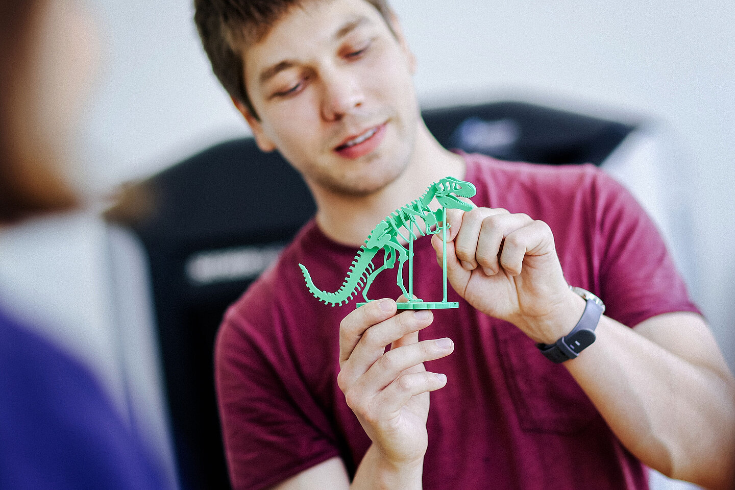 Nahaufnahme eines Mannes, der ein grünes Skelettmodell eines Dinosauriers mit beiden Händen präsentiert.