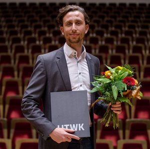 Der Preisträger Max Vollmering mit dem Dissertationspreis und einem Blumenstrauß in der Hand haltend im Gewandhaus zu Leipzig Der Preisträger Max Vollmering hält die Urkunde des Dissertationspreises in der einen Hand und einen Blumenstrauß in der anderen.