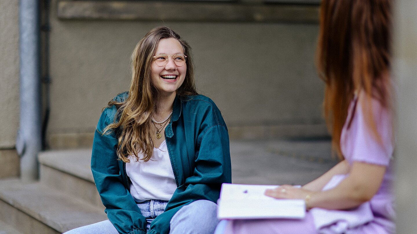 Freudestrahlende junge Frau auf den Eingangstreppen zu einem HTWK-Gebäude