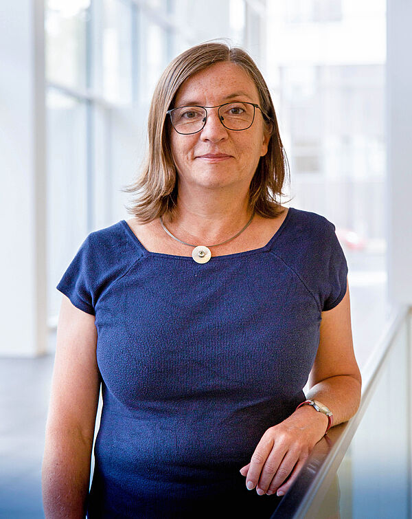 Ein Portraitfoto einer stehenden Frau mit blauem Oberteil