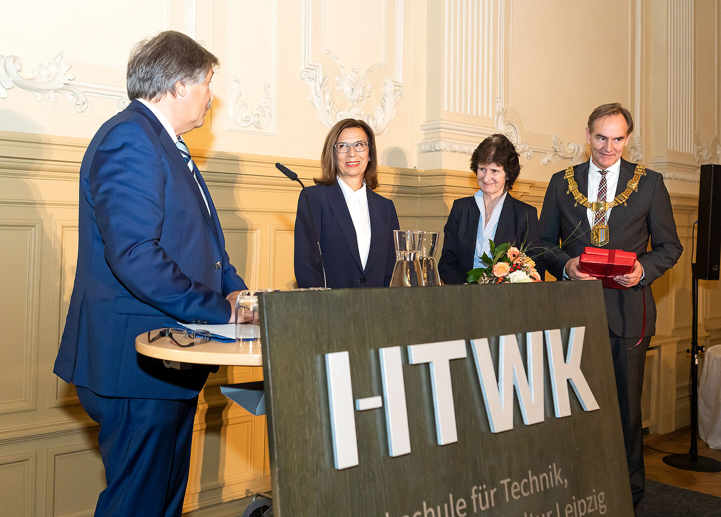 Danken Amtsvorgängerin Prof. Gesine Grande (2.v.l.): Der Hochschulratsvorsitzende Dr.-Ing. Matthias Reuschel (li.), die sächsische Staatministerin Dr. Eva-Maria Stange und Leipzigs OBM Burkhard Jung. (Foto: Swen Reichhold/HTWK Leipzig) Vier Personen auf der Bühne mit Pult „HTWK“.