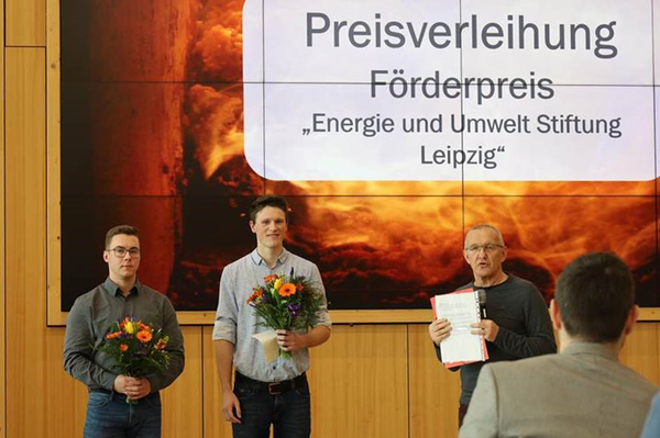 Preisträger und Preisverleiher mit Blumen und Urkunde